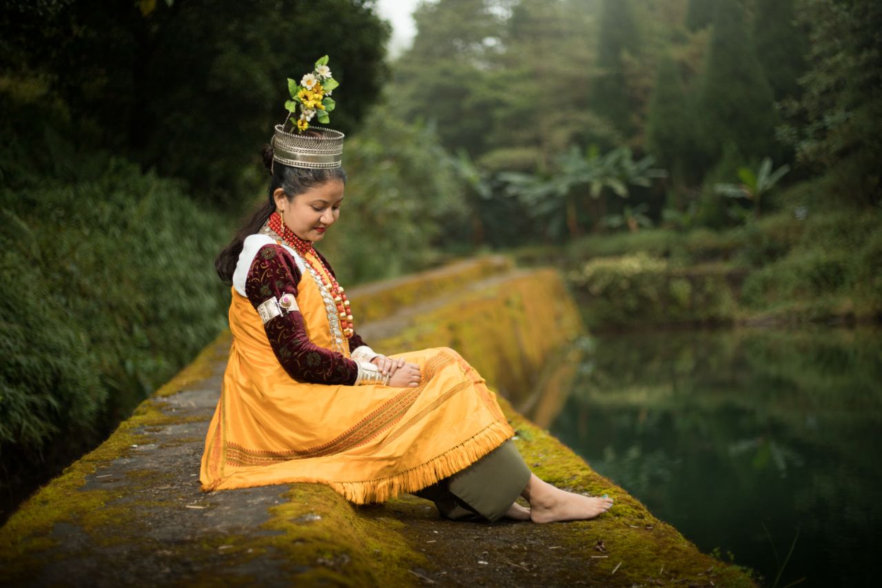 A woman sitting at the edge of a lake wearing Khasi ceremonial dress